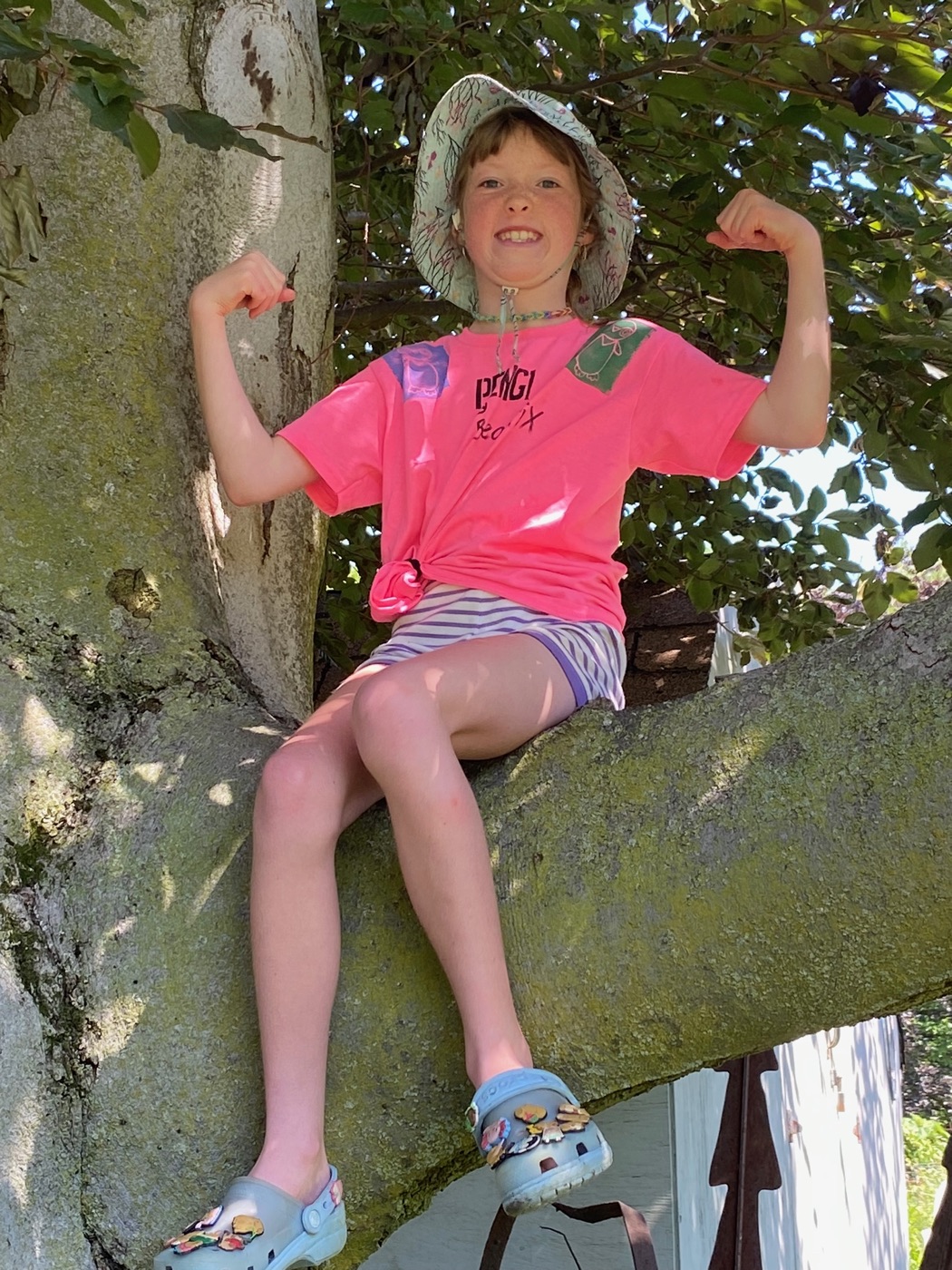 Kid flexing in a tree wearing a pink Pengi shirt