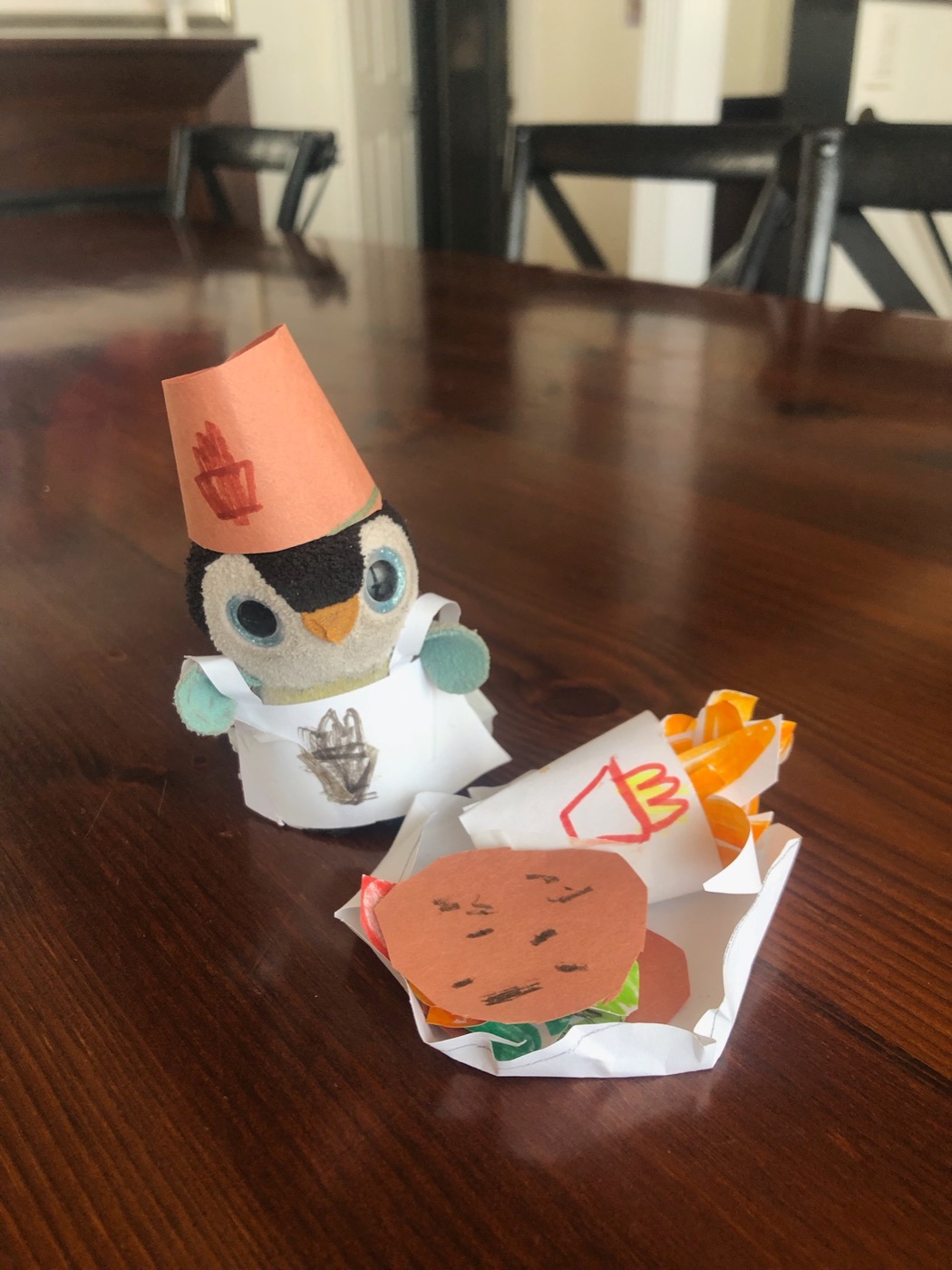 Pengi in a paper chef hat serving a paper burger and fries