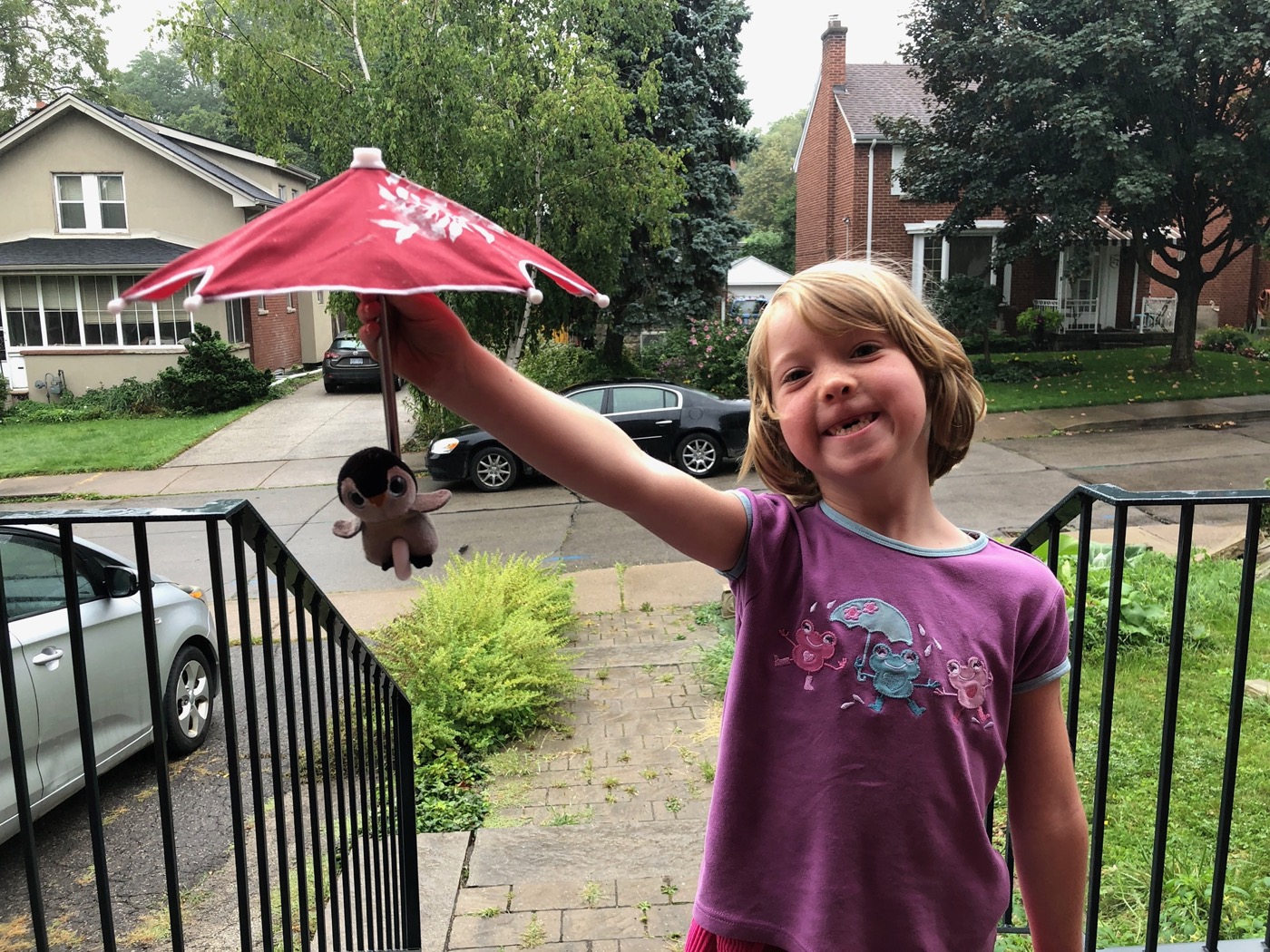 Beatrix on the front steps holding a tiny umbrella over Pengi